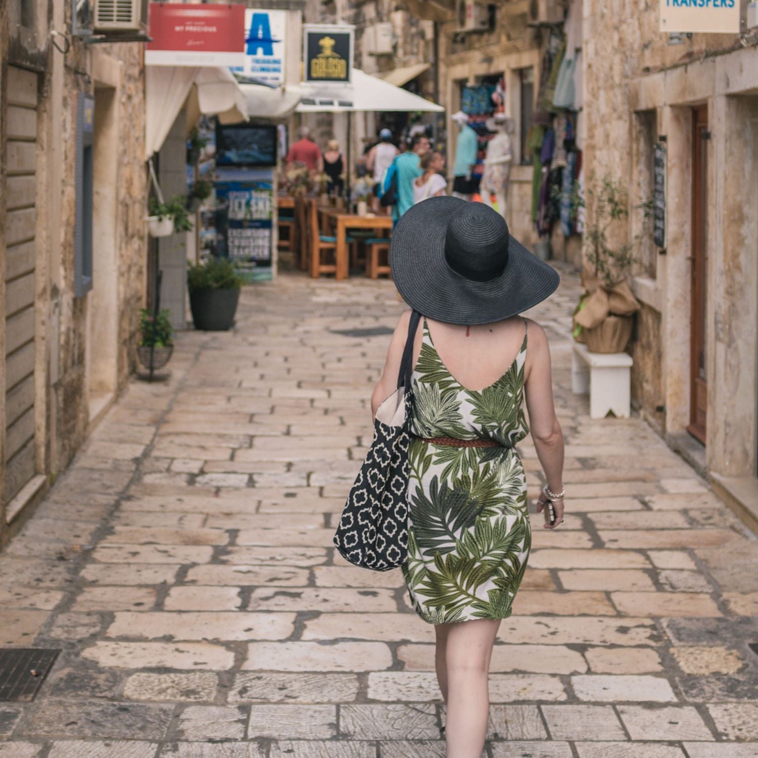 A woman in a green summer dress walks toward shops