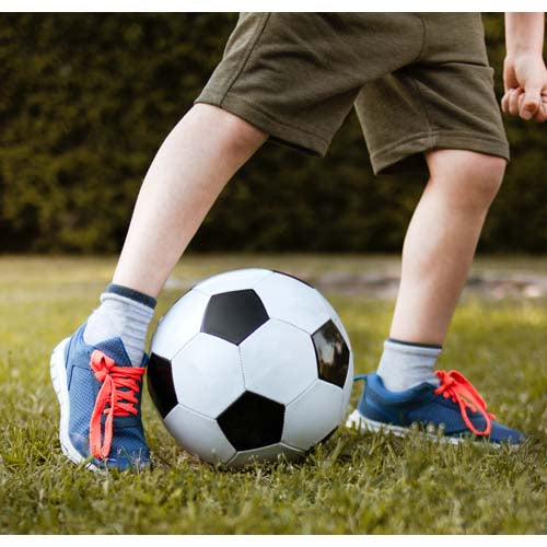 Below waist young boy in shorts with football at feet